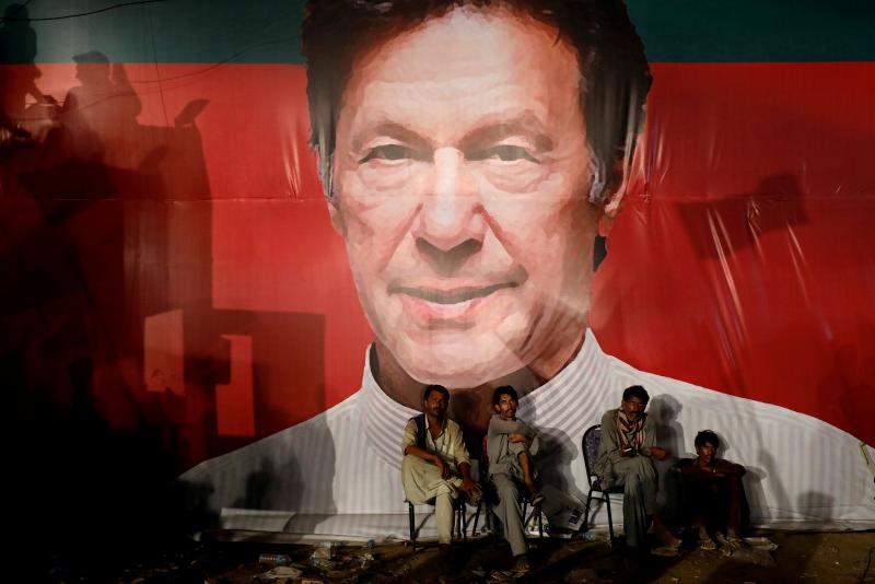 Labourers, who set up the venue, sit under a wall with a billboard displaying a photo of Imran Khan, chairman of the Pakistan Tehreek-e-Insaf (PTI), political party, as they listen to him during a campaign rally ahead of general elections in Karachi, Pakistan July 22, 2018. REUTERS