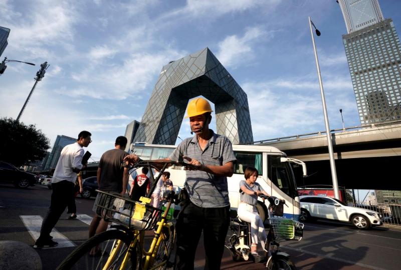 A construction worker walks with an Ofo`s shared bike near the China Central Television (CCTV) building (behind) in Beijing`s central business district, China August 16, 2018. REUTERS/FILE PHOTO