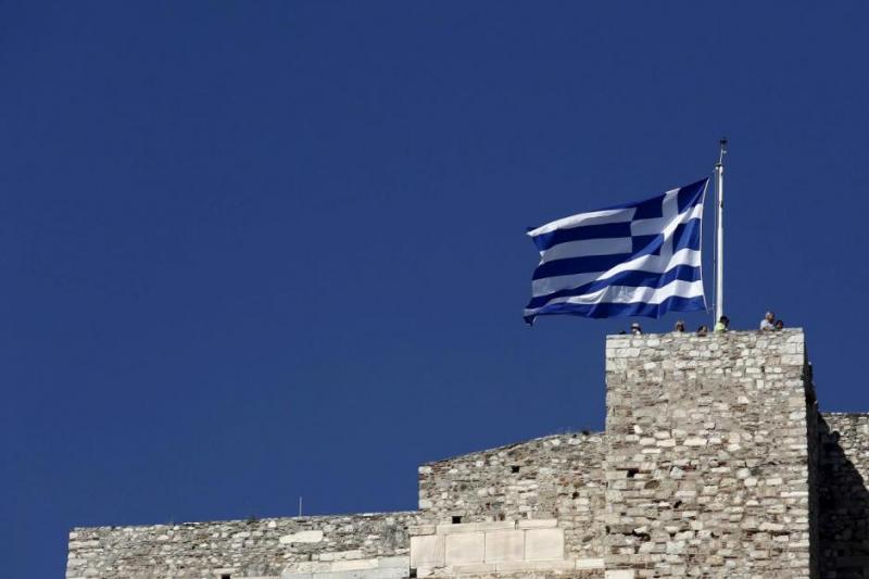 Tourists stand under a Greek national flag atop the Acropolis hill in Athens, June 14, 2015. REUTERS