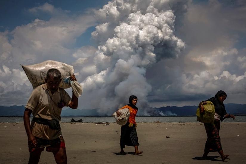 Smoke is seen on the Myanmar border as Rohingya refugees walk on the shore after crossing the Bangladesh-Myanmar border by boat through the Bay of Bengal, in Shah Porir Dwip, Bangladesh September 11, 2017. REUTERS