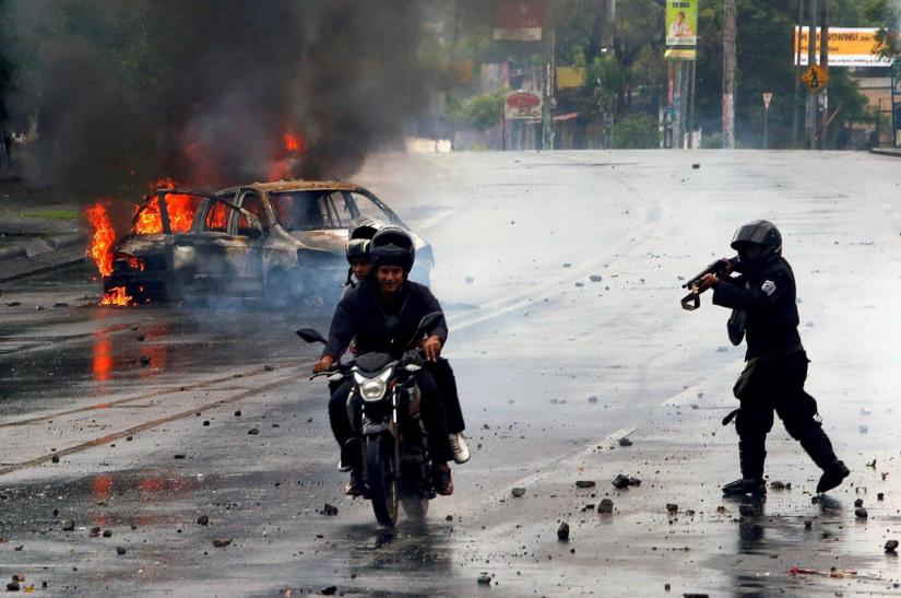 A riot police officer fires his shotgun towards two men during a protest against Nicaragua`s President Daniel Ortega`s government in Managua, Nicaragua May 28, 2018. REUTERS/file photo