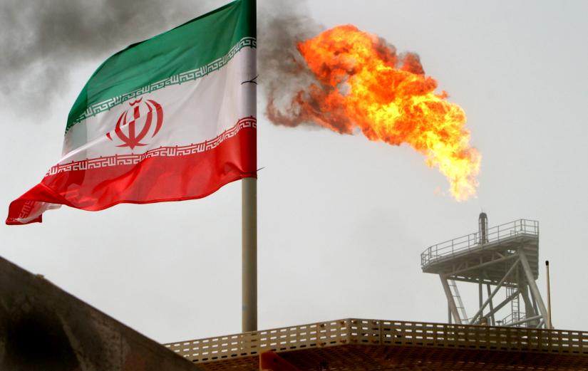A gas flare on an oil production platform in the Soroush oil fields is seen alongside an Iranian flag in the Persian Gulf, Iran, July 25, 2005.   REUTERS FILE PHOTO