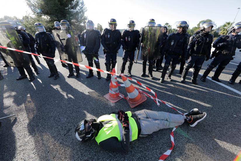 French CRS police secure a position as a man wearing a yellow vest, a symbol of a French drivers` protest against higher fuel prices, lays on the road in Antibes, France, November 17, 2018. REUTERS
