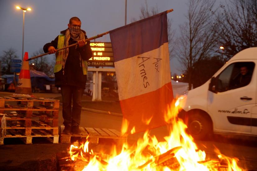 A protester wearing a yellow vest, the symbol of a French drivers` protest against higher diesel fuel prices, holds a flag near burning debris at the approach to the A2 Paris-Brussels Motorway, in Fontaine-Notre-Dame, France, December 4, 2018. REUTERS