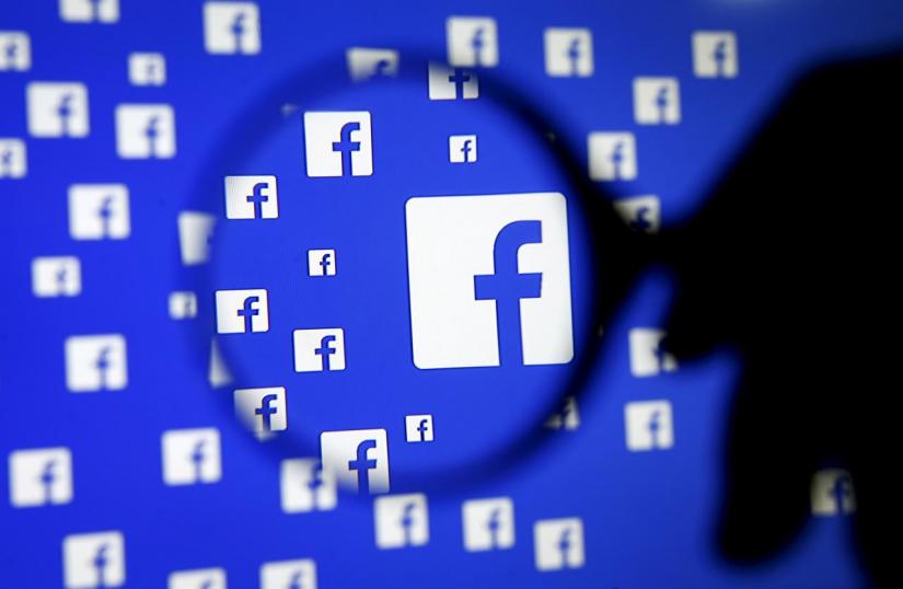 A man poses with a magnifier in front of a Facebook logo on display in this illustration taken in Sarajevo, Bosnia and Herzegovina, December 16, 2015. REUTERS/FILE PHOTO