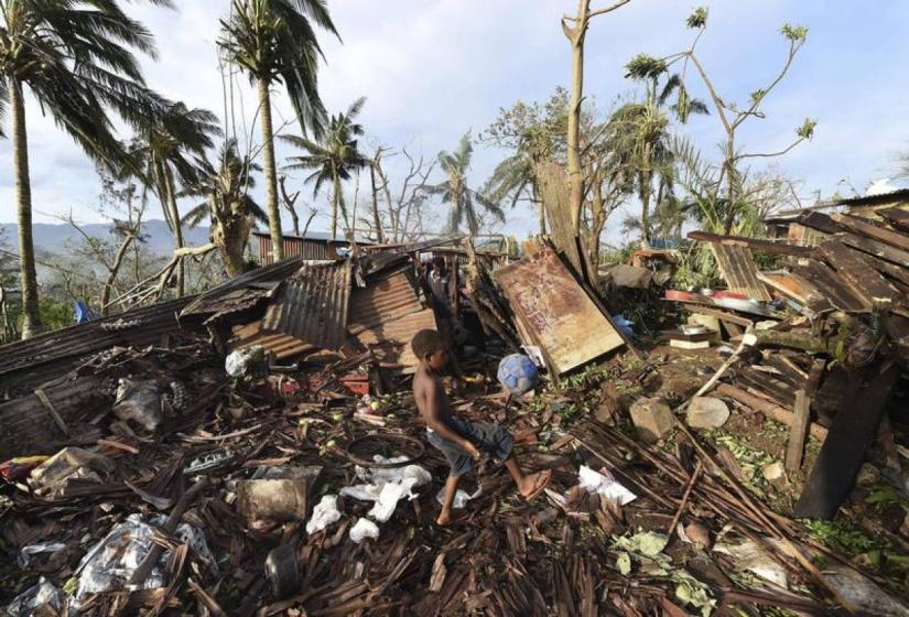 A boy called Samuel kicks a ball as his father Phillip searches through the ruins of their home which was destroyed by Cyclone Pam in Port Vila, the capital city of the Pacific island nation of Vanuatu, March 16, 2015. REUTERS