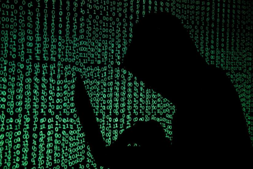 A hooded man holds a laptop computer as cyber code is projected on him in this illustration picture taken on May 13, 2017. REUTERS