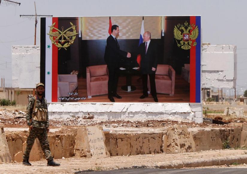 A soldier stands guard near a poster of Syria`s Bashar al-Assad and Russia`s Vladimir Putin during the re-opening of the road between Homs and Hama in Rastan, Syria, June 6, 2018. REUTERS