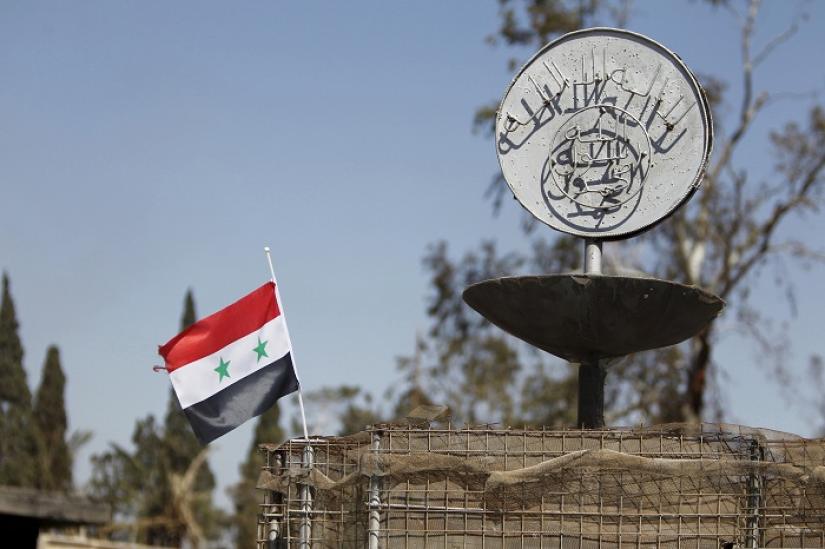 A Syrian national flag flutters next to the Islamic State`s slogan at a roundabout where executions were carried out by ISIS militants in the city of Palmyra, in Homs Governorate, Syria in this April 1, 2016. Reuters/File Photo