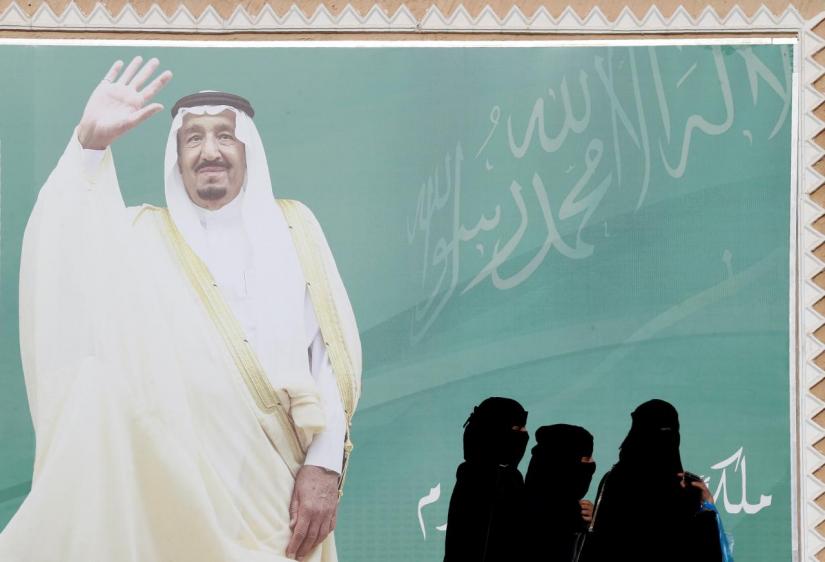 Women walk past a poster of Saudi Arabia`s King Salman bin Abdulaziz Al Saud during Janadriyah Cultural Festival on the outskirts of Riyadh, Saudi Arabia February 12, 2018. REUTERS