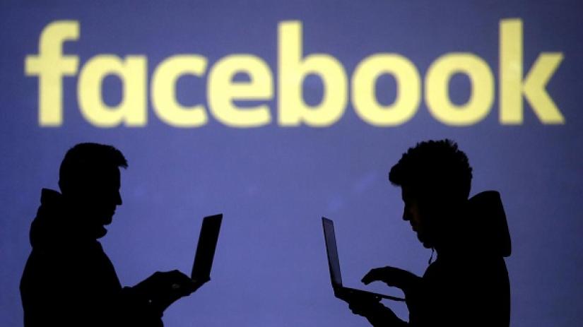 Silhouettes of laptop users are seen next to a screen projection of Facebook logo in this picture illustration taken March 28, 2018. REUTERS/Illustration/File Photo