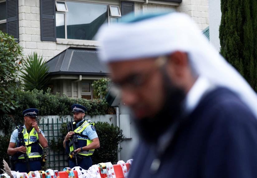 Police officers stand guard as a Muslim man passes near a memorial site of Friday`s shooting, outside Al Noor mosque in Christchurch, New Zealand March 19, 2019. REUTERS