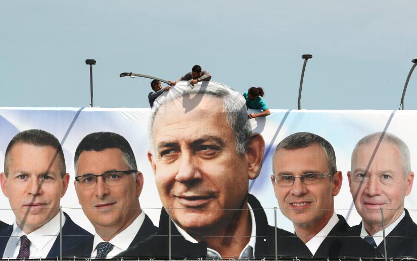 Labourers work on hanging up a Likud election campaign banner depicting Israeli Prime Minister Benjamin Netanyahu with his party candidates, in Jerusalem