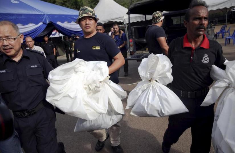 Forensic policemen carry body bags with human remains found at the site of human trafficking camps.