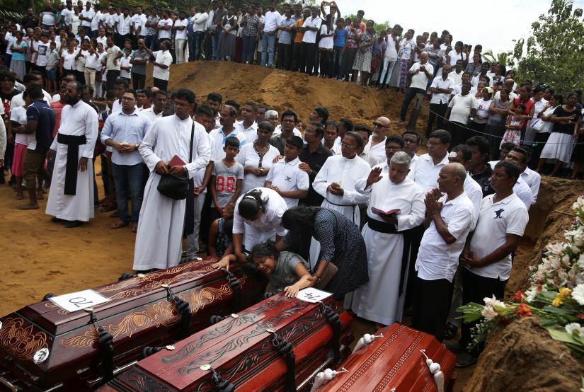 A woman reacts next to two coffins during a mass burial of victims, two days after a string of suicide bomb attacks o