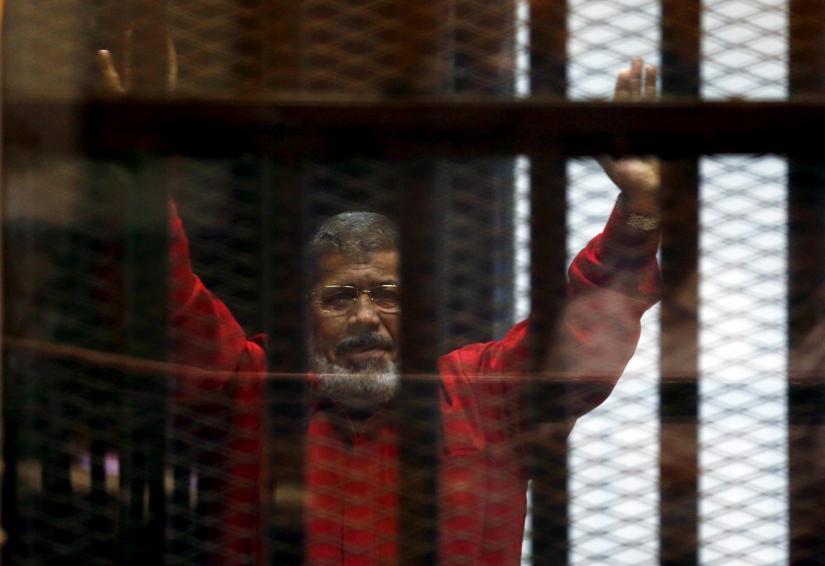 FILE PHOTO: Egypt`s deposed president Mohamed Mursi greets his lawyers and people from behind bars at a court wearing the red uniform of a prisoner sentenced to death, during his court appearance with Muslim Brotherhood members on the outskirts of Cairo, Egypt, June 21, 2015. REUTERS