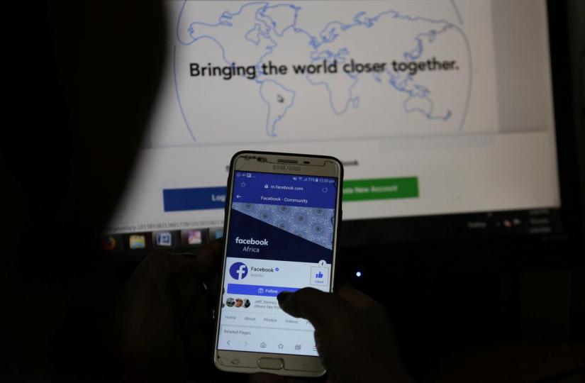 An illustration photo shows the Facebook page displayed on a mobile phone internet browser held in front of a computer screen at a cyber-cafe in downtown Nairobi, Kenya April 18, 2019. REUTERS/File Photo