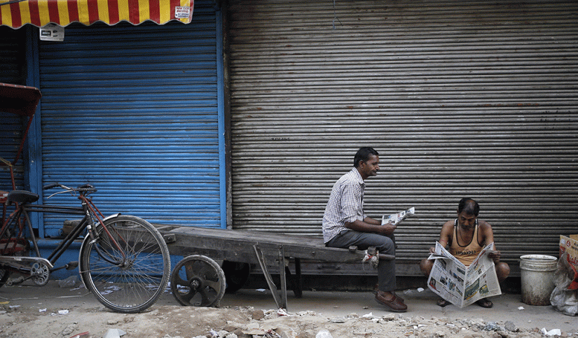 Labourers read newspapers in front of a closed shop in the old quarters of Delhi, India, March 29, 2016. Reuters/File Photo