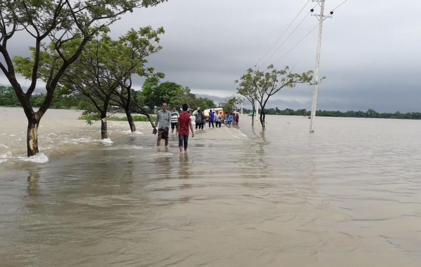 People walking in knee-deep water as flash floods and rainfall inundated low-lying areas in Sunamganj