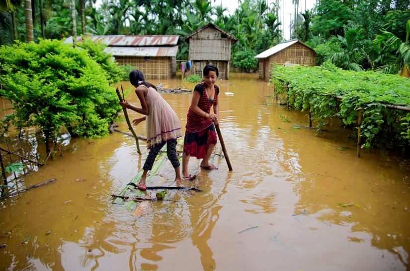 Girls row a makeshift raft past submerged houses at a flood-affected village in Karbi Anglong district, in the northeastern state of Assam, India, July 11, 2019. REUTERS/File Photo
