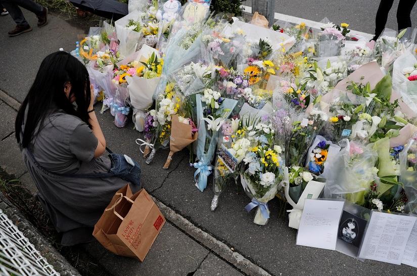 A woman prays in front of a row of flowers placed for victims of the torched Kyoto Animation building in Kyoto, Japan, July 20, 2019. REUTERS