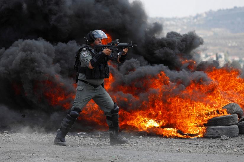 An Israeli border police member aims his weapon as he stands next to burning tires during a Palestinian protest against the nearby Jewish settlement of Qadomem, in the village of Kofr Qadom in the Israeli-occupied West Bank July 19, 2019. REUTERS