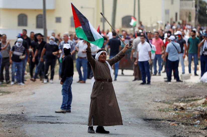 A demonstrator holds a Palestinian flag and a cane during a protest against the nearby Jewish settlement of Qadomem, in the village of Kofr Qadom in the Israeli-occupied West Bank July 19, 2019. REUTERS