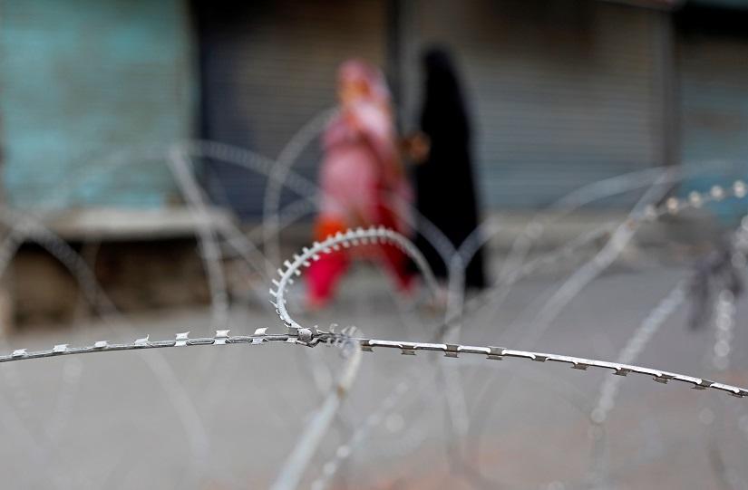 Kashmiri women walk past concertina wire laid across a road during restrictions after the scrapping of the special constitutional status for Kashmir by the Indian government, in Srinagar, August 20, 2019. REUTERS