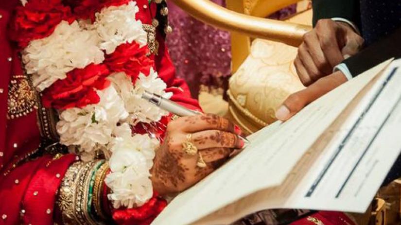 The representational image shows a woman signing a marriage contract.