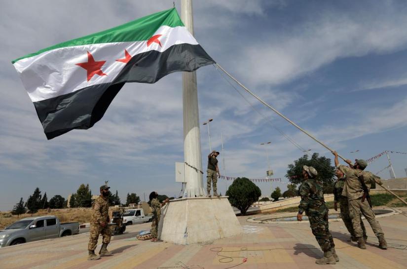 FILE PHOTO: Turkey-backed Syrian rebel fighters raise the Syrian opposition flag at the border town of Tel Abyad, Syria, Oct 14, 2019. REUTERS
