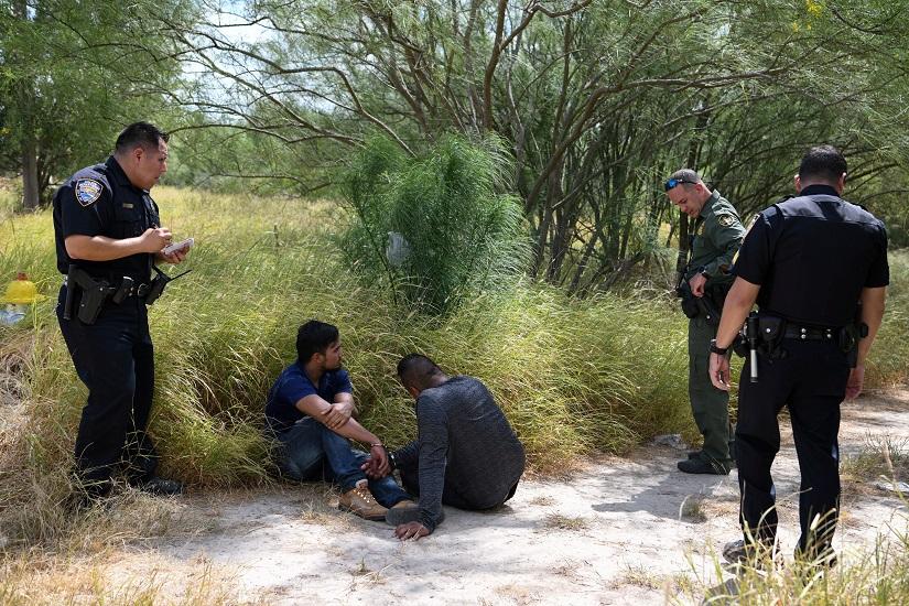 FILE PHOTO: Migrant men sit on the ground after being detained by law enforcement for illegally crossing the Rio Grande and attempting to evade capture in Hidalgo, Texas, US, Aug 23, 2019. REUTERS