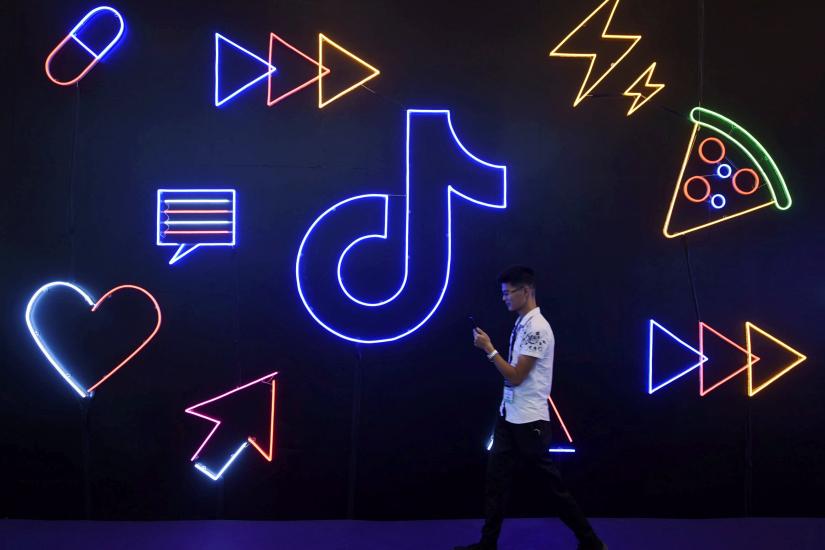 A man holding a phone walks past a sign of Chinese company ByteDance`s app TikTok, known locally as Douyin, at the International Artificial Products Expo in Hangzhou, Zhejiang province, China October 18, 2019. REUTERS