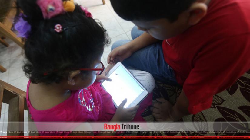 Two kids are seen playing with an electronic device. 