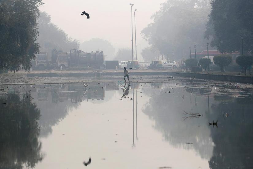 A man cleans a pond on a smoggy morning in New Delhi, Nov 11, 2019. REUTERS