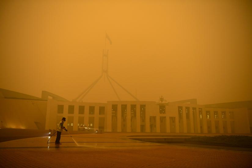 A man cleans the forecourt of Parliament House surrounded by smoke haze early morning in Canberra, Sunday, January 5, 2020. AAP Image via REUTERS