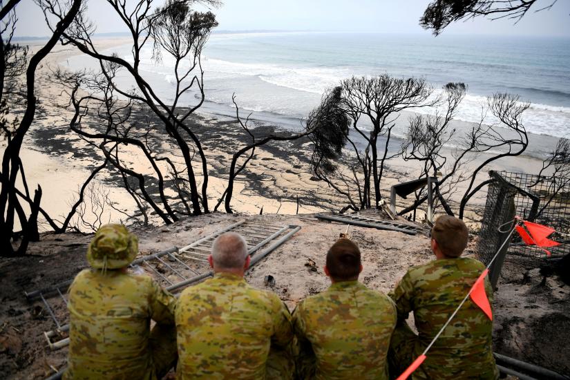 Soldiers sit on a beach amongst burnt trees where people had previously taken shelter during a fire on New Year`s Eve in Mallacoota, Australia January 10, 2020. REUTERS