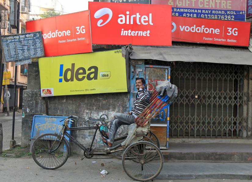 A rickshaw puller speaks on his mobile phone as he waits for customers in front of advertisement billboards belonging to telecom companies in Kolkata February 3, 2014. REUTERS/File Photo