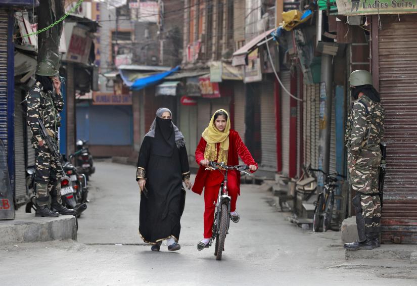 A Kashmir girl rides her bike past Indian security force personnel standing guard in front of closed shops on a street in Srinagar, Oct. 30, 2019. FILE PHOTO