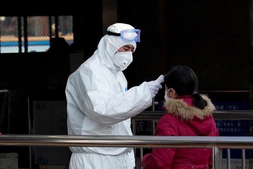 A worker takes the body temperature of a passenger before she enters the subway station outside the Beijing Railway Station in central Beijing, Jan 25, 2020. REUTERS