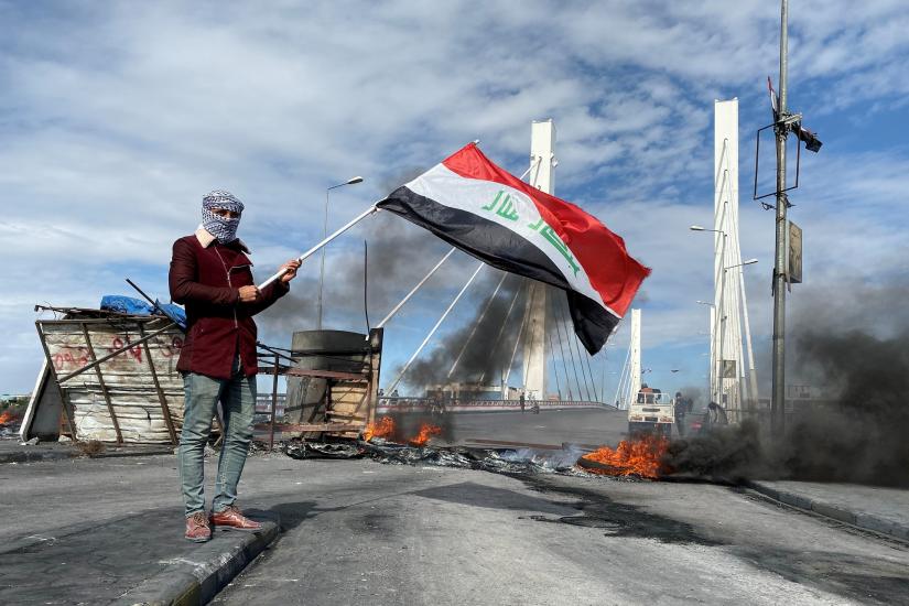 A demonstrator holds Iraqi flag near burning tires blocking a road, during ongoing anti-government protests in Nassiriya, Iraq January 25, 2020. REUTERS