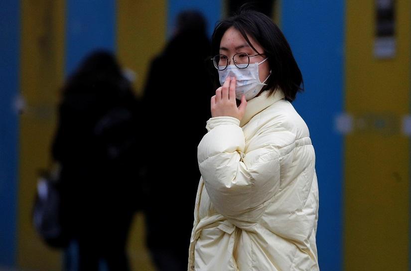 A woman wears a face mask as she crosses a road in the Chinatown area of Manchester, Britain Jan 27 2020. REUTERS