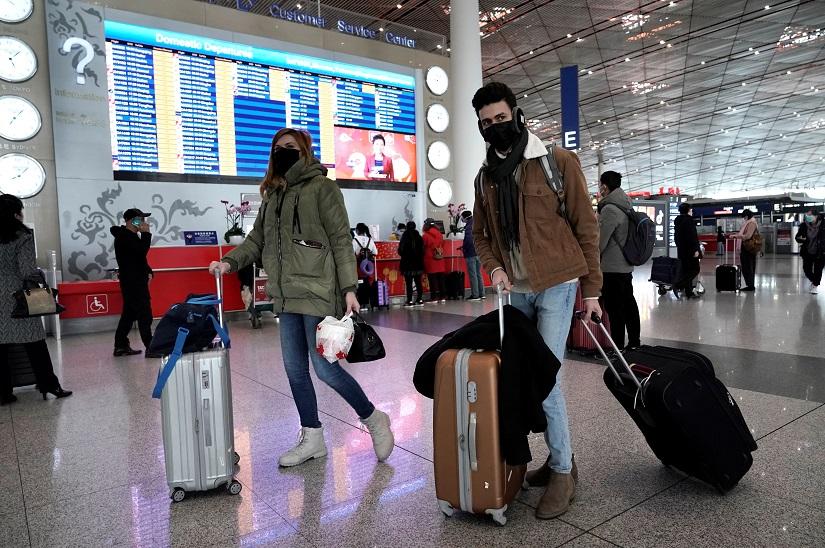 Foreign travellers wearing masks walk past a departures information board at Beijing International Airport in Beijing, China as the country is hit by an outbreak of the new coronavirus, Feb 1, 2020. REUTERS