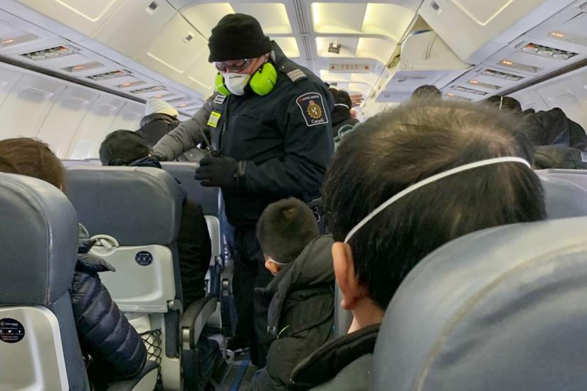 A Royal Canadian Mounted Police (RCMP) officer wearing a mask checks Canadians, who had been evacuated from China on an American charter plane due to the outbreak of novel Coronavirus, on another aircraft taking them to Canadian Forces Base (CFB) Trenton, from Vancouver International Airport in Richmond, British Columbia, Canada, February 7, 2020. Courtesy of Edward Wang via REUTERS.