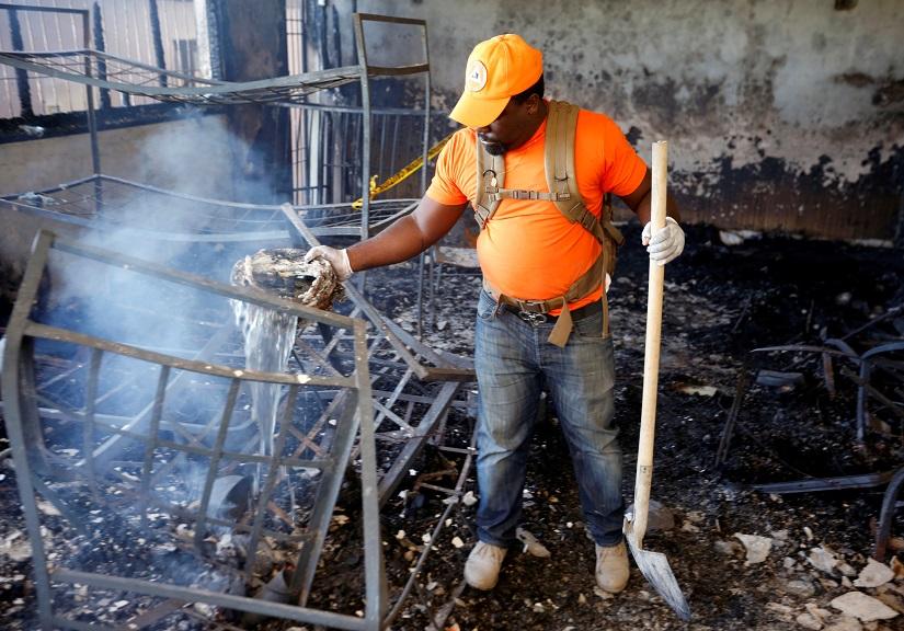 A civil protection worker pours water over burning debris inside a bedroom at an orphanage after it was destroyed in a fire, in Port-au-Prince, Haiti Feb 14, 2020. REUTERS