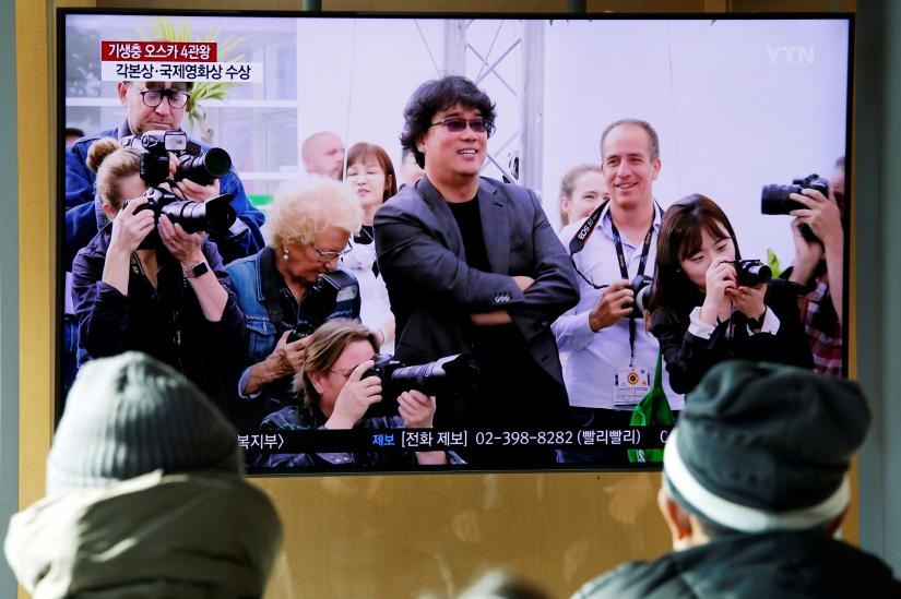 FILE PHOTO: People watch a TV broadcasting a news report on South Korean director Bong Joon-ho who won four Oscars with his film `Parasite`, in Seoul, South Korea, February 10, 2020. REUTERS