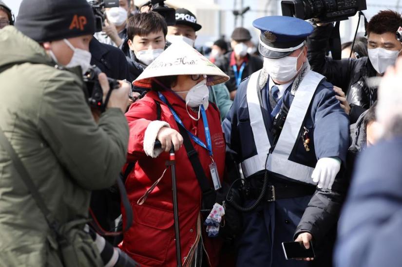 A police officer escorts a passenger away from the media as she walks out from the cruise ship Diamond Princess at Daikoku Pier Cruise Terminal in Yokohama, south of Tokyo, Japan Feb 19, 2020. REUTERS
