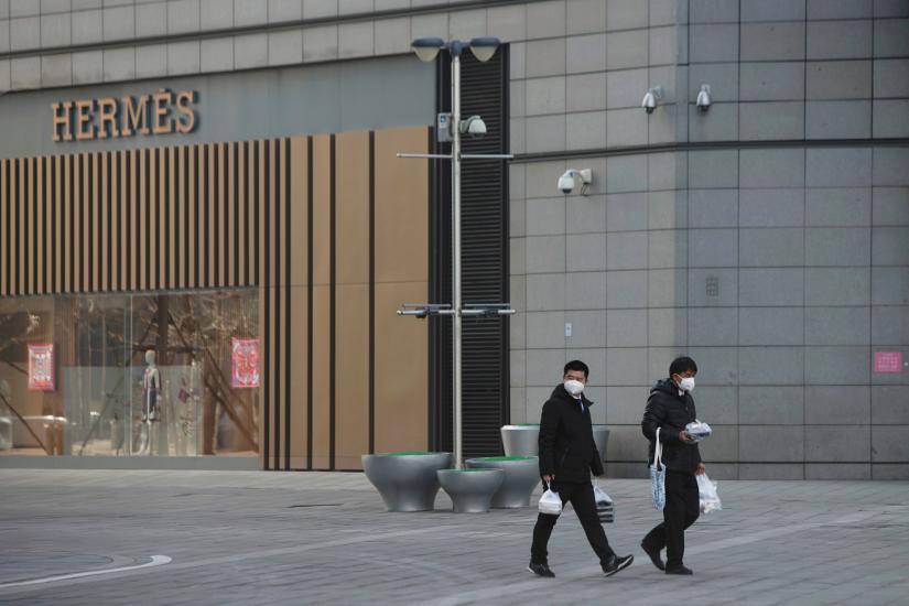 Men wearing face masks walk with takeaway food past a Hermes store at a shopping centre after the extended Lunar New Year holiday caused by the novel coronavirus outbreak, in Beijing's central business district, China February 10, 2020. REUTERS
