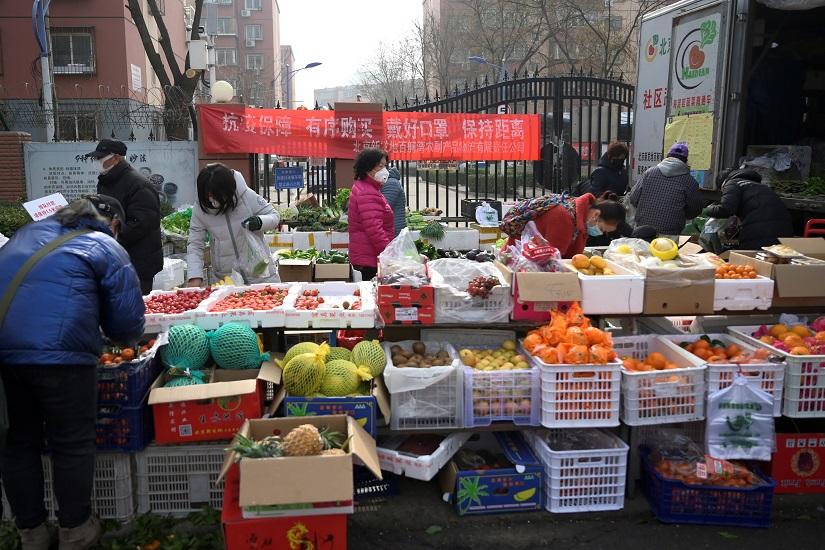 Residents wearing face masks buy food at a grocery stall that is set up outside a residential compound following an outbreak of the novel coronavirus in the country, in Beijing, China February 21, 2020. The banner reads, `Protection against epidemic, make purchases orderly, wear face masks, keep a distance`. REUTERS