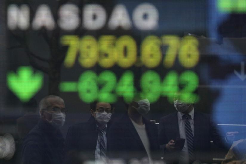 People wearing protective face masks, following an outbreak of the coronavirus disease (COVID-19), are reflected in a screen displaying NASDAQ movements outside a brokerage in Tokyo, Japan, March 10, 2020. REUTERS