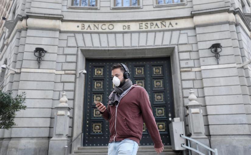 FILE PHOTO: A man wears a protective face mask as he walks past Banco de Espana (Bank of Spain), amidst concerns over coronavirus outbreak, in Barcelona, Spain Mar 14, 2020. REUTERS